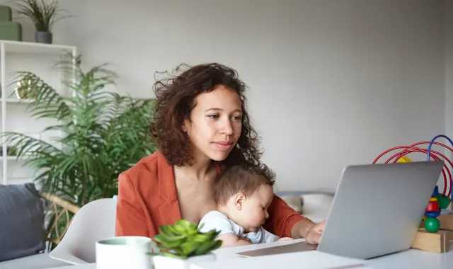 Online nursing student working on a computer with a child on her lap